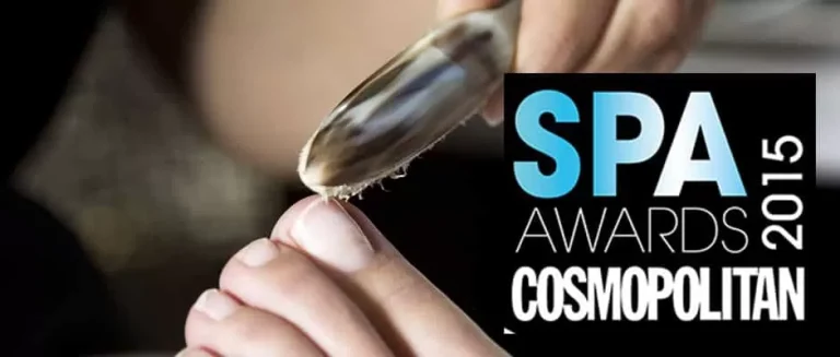 Close-up of a person receiving a pedicure with a metallic tool scraping the skin on their toe. Overlaid text reads "SPA AWARDS 2015 COSMOPOLITAN" in different fonts and colors.