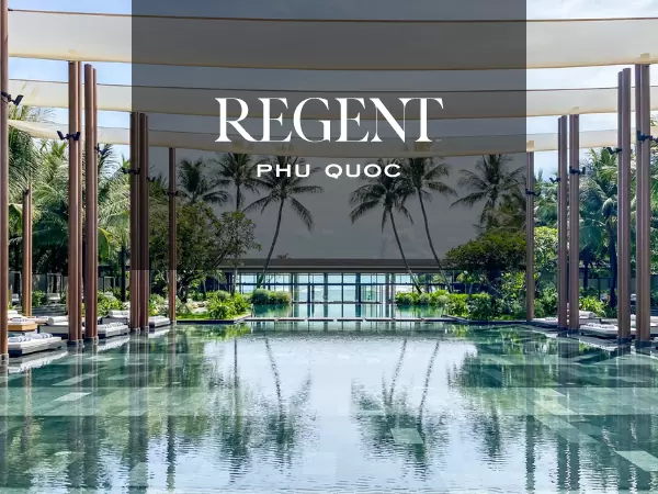 Luxurious pool area at Regent Phú Quốc with crystal-clear water reflecting palm trees and modern architecture. The backdrop features lush greenery and clear skies, evoking a sense of relaxation and tropical elegance.
