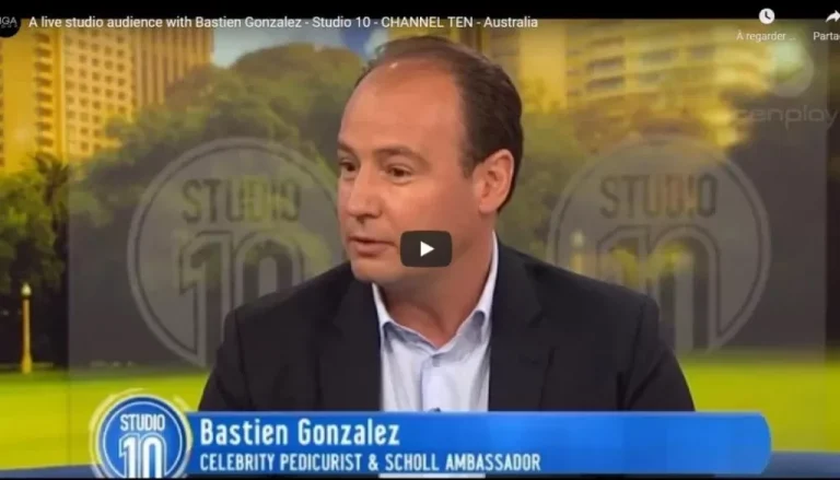 A man is speaking in a TV studio, wearing a dark suit jacket and light blue shirt. The background shows a blurred "Studio 10" logo. A banner at the bottom reads, "Bastien Gonzalez, Celebrity Pedicurist & Scholl Ambassador.
