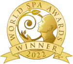 An award medallion with a gold circular design featuring the profile of a human face and a spiral shape. The outer circle is labeled "World Spa Awards," and a ribbon at the bottom reads "Winner 2022".