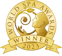 A gold circular badge featuring a stylized human figure with outstretched arms, encircled by the text "World Spa Awards". Below the figure is a ribbon that reads "Winner 2023".