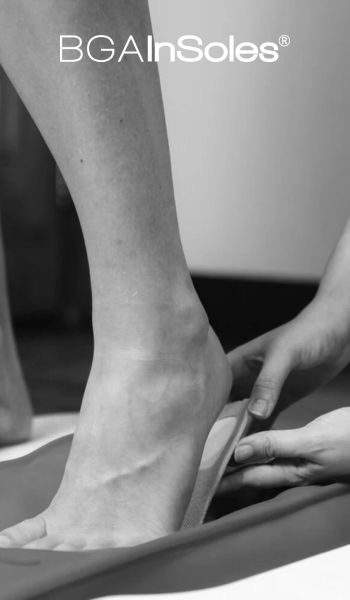 Image en noir et blanc du pied d'une personne mesuré ou ajusté pour une semelle intérieure par les mains d'une autre personne. Le texte « BGAInSoles® » est affiché bien en vue en haut de l'image.